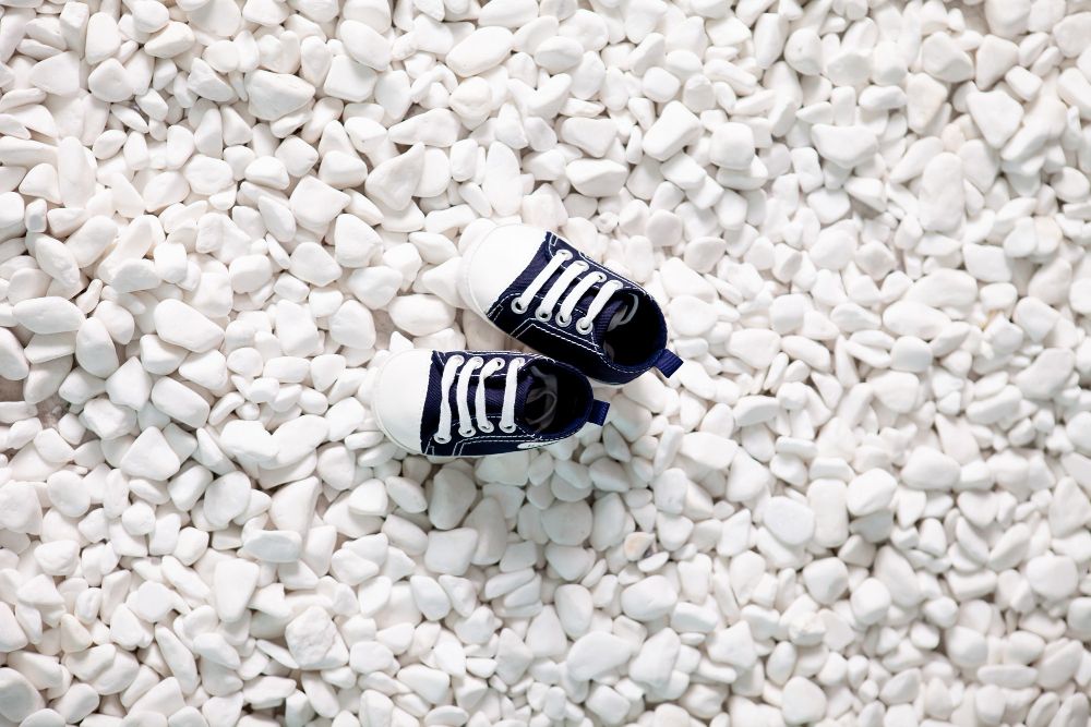 Imagen de grava canto rodado blanco sobre una superficie plana. Las piedras son de diferentes tamaños y formas, con un color blanco puro y una textura suave. Algunas de las piedras tienen vetas grises o beige. El fondo de la imagen es de color marrón claro.